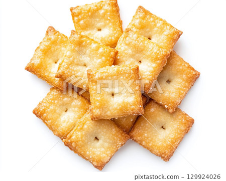 A close-up shot of a small pile of square creme crackers stacked against a plain white background. The crackers are golden-brown with small holes on their surface. 129924026