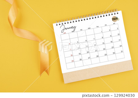 January 2026 desk calendar with yellow ribbon on yellow color background, Flat lay. January 2026 desk calendar with yellow ribbon on yellow color background, Flat lay. 129924030