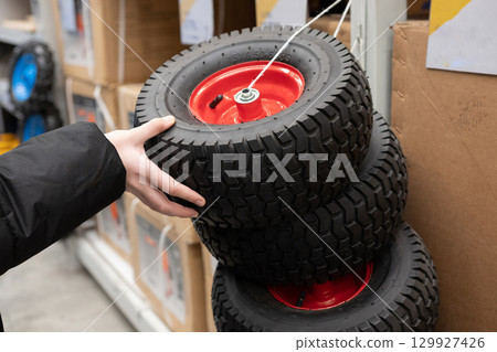 Individual examining multiple tires with red rims in a retail store during daytime hours 129927426