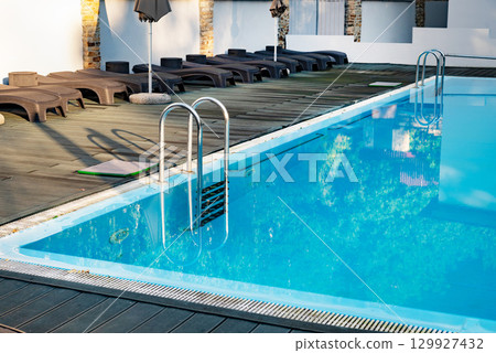 Outdoor swimming pool with metal ladder and lounge chairs around. Outdoor swimming pool with metal ladder and lounge chairs around. 129927432