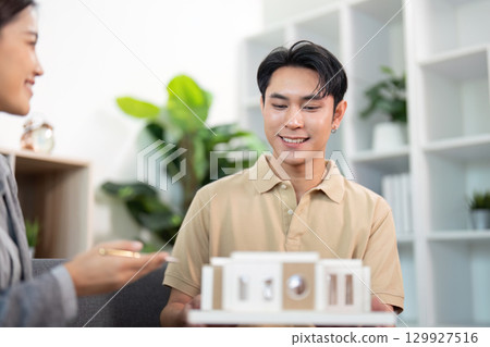 Real Estate Agent Smiling with Client Over Model House Real Estate Agent Smiling with Client Over Model House 129927516