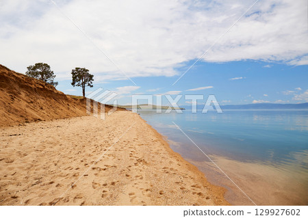 The shore of Lake Baikal on a cloudy summer day. Calm blue water, sandy beach. 129927602