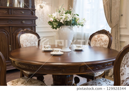 Round wooden table with four chairs around it. Contemporary interior design furnishings arrangement. Home decor, cafe, restaurant furniture concept. Elegant luxurious dining set in classic rich style. 129928344