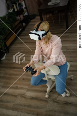 Engaging in virtual reality gaming at home while seated on a stylish chair during an afternoon session 129928999