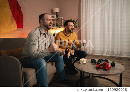 Excitement fills the room as two friends cheer for their favorite team during a big match night 129929028