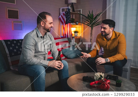 Two friends share stories and laughter over drinks in a cozy living room filled with warm ambiance and American decor 129929033
