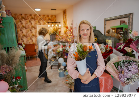 Flower shop vibrancy with cheerful florist showcasing bright blossoms in a cozy space 129929077
