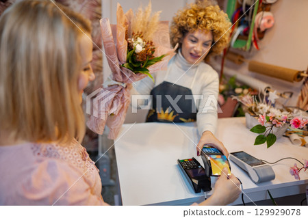 Inside a charming flower shop, a cheerful sales associate assists a customer with a lovely bouquet 129929078