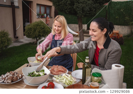 Friends create delicious meals together in a sunny backyard kitchen Friends create delicious meals together in a sunny backyard kitchen 129929086