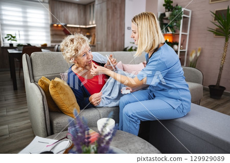 Caring interaction between a nurse and an elderly woman in a cozy living room 129929089
