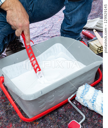 House painter worker prepares white paint. Building. 129929145