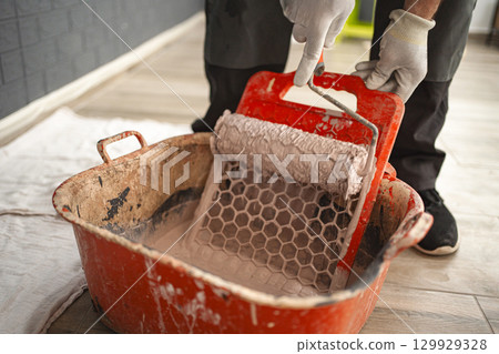 Man dips a paint roller to wipe off the excess paint on the squeegee Man dips a paint roller to wipe off the excess paint on the squeegee 129929328