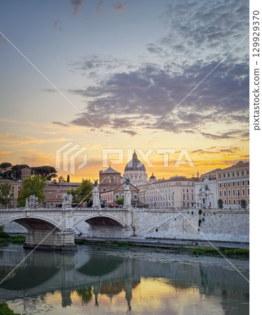 Scenic sunset over the Tiber River in Rome. The Ponte Sant'Angelo visible in the foreground with Saint Peter's Basilica in background. The colorful sky and city buildings reflects in the calm waters Scenic sunset over the Tiber River in Rome. The Ponte Sant'Angelo visible in the foreground with Saint Peter's Basilica in background. The colorful sky and city buildings reflects in the calm waters 129929370