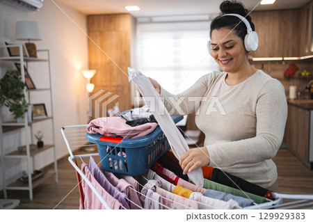 Woman listening to music while hanging the laundry on drying rack at home Woman listening to music while hanging the laundry on drying rack at home 129929383