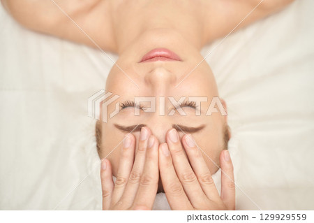 Relaxed caucasian young female receiving facial massage at spa wellness center 129929559