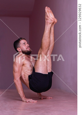 Athletic man holds advanced core balance on hands with legs lifted. Concept of strength, focus, discipline, control, endurance and body mastery. 129929632