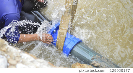 A plumber is repairing a large water pipe that is leaking badly. A plumber is repairing a large water pipe that is leaking badly. 129930177