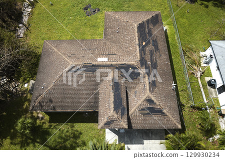Damaged house roof with missing shingles after hurricane Ian in Florida. Consequences of natural disaster Damaged house roof with missing shingles after hurricane Ian in Florida. Consequences of natural disaster 129930234