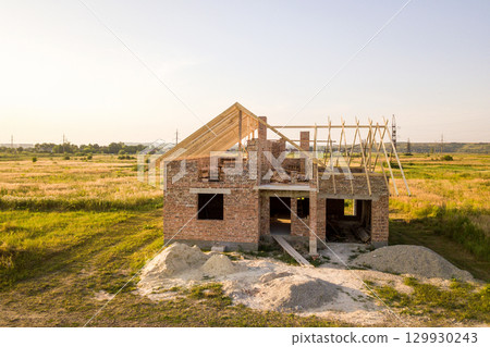 Unfinished brick house with wooden roof structure under construction. 129930243
