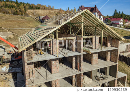 Wooden frame of new roof on a brick big house under construction. 129930289