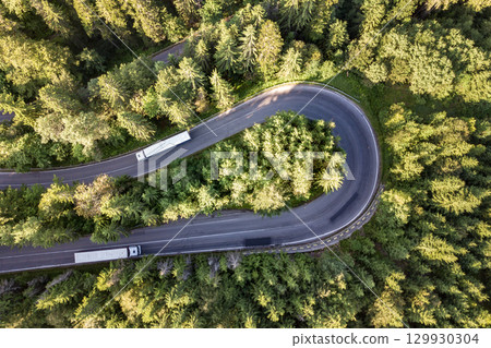 Aerial view of winding road in high mountain pass trough dense green pine woods. Aerial view of winding road in high mountain pass trough dense green pine woods. 129930304