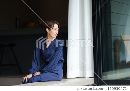 A woman sitting on a terrace looking out at the garden 129930471