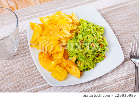 Beer snacks are laid out on plate - chips and portion of thick pasta sauce guacamole 129930989