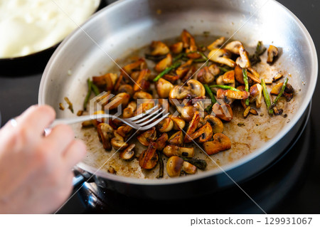 Finely chopped champignons and young asparagus shoots are fried in frying pan. Finely chopped champignons and young asparagus shoots are fried in frying pan. 129931067