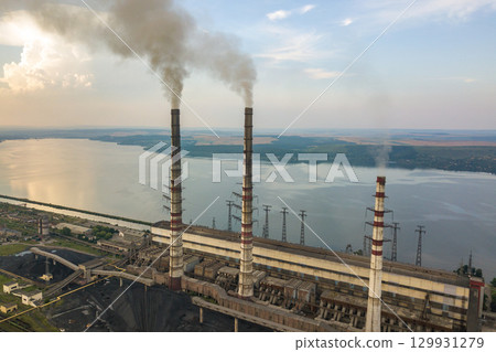 Aerial view of high chimney pipes with grey smoke from coal power plant. Production of electricity with fossil fuel. 129931279