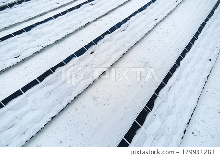 Aerial view of snow covered sustainable electric power plant with rows of solar photovoltaic panels for producing clean electrical energy. Low effectivity of renewable electricity in northern winter 129931281