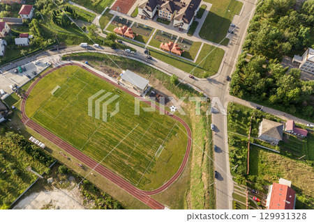 Aerial view of a football field on a stadium covered with green grass in rural town area. 129931328