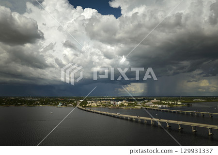 Heavy thunderstorm approaching traffic bridge connecting Punta Gorda and Port Charlotte over Peace River. Bad weather conditions for driving during rainy season in Florida 129931337
