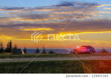 Tourist camping tents and off road car on mountain campsite at bright sunny evening. Active tourism and offroad driving adventure concept Tourist camping tents and off road car on mountain campsite at bright sunny evening. Active tourism and offroad driving adventure concept 129931347