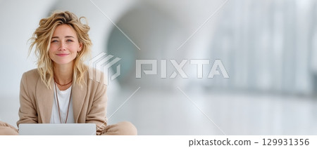A Happy Smiling Woman is Working on Her Laptop in a Stylish Modern Workspace Setting 129931356