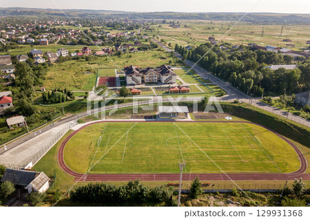 Aerial view of a football field on a stadium covered with green grass in rural town area. 129931368