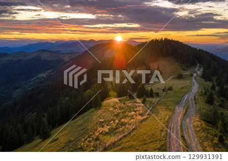 Mountain landscape of trekking route. Dark dirt road between spruce woods illuminated with yellow setting sun. Bright colorful sunset in wild national park highlands Mountain landscape of trekking route. Dark dirt road between spruce woods illuminated with yellow setting sun. Bright colorful sunset in wild national park highlands 129931391