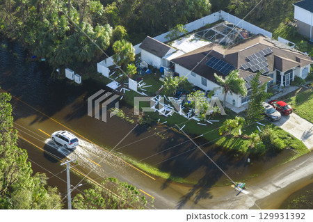 Flooded Florida road with evacuating cars and surrounded with water houses in suburban residential area. Consequences of hurricane natural disaster 129931392