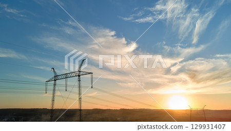 Dark silhouette of high voltage tower with electric power lines at sunrise. Transmission of electric energy concept Dark silhouette of high voltage tower with electric power lines at sunrise. Transmission of electric energy concept 129931407