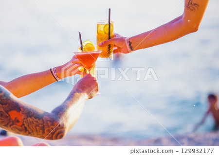 Group of friends clinking glasses with cocktails on the beach. Tattoos on arms Group of friends clinking glasses with cocktails on the beach. Tattoos on arms 129932177