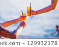 Group of friends clinking glasses with cocktails on the beach. Tattoos on arms 129932178