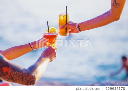 Group of friends clinking glasses with cocktails on the beach. Tattoos on arms 129932178