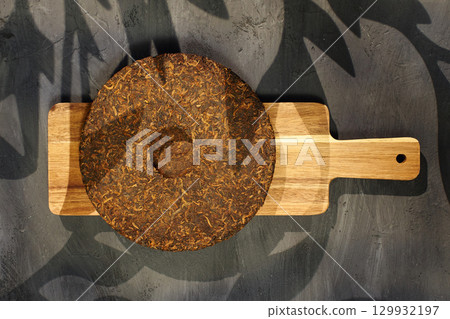 Puer tea is showcased on a wooden cutting board, highlighting its circular shape and compressed leaves. Puer tea is showcased on a wooden cutting board, highlighting its circular shape and compressed leaves. 129932197
