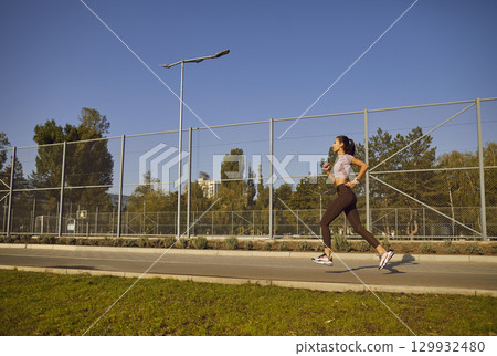 Woman running along a wire fence during an outdoor morning workout in the summer 129932480
