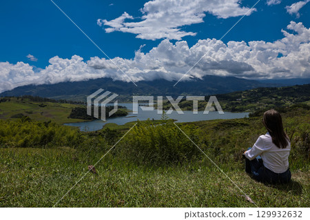 Female tourist sitting looking at the biggest artificial lake in Colombia called Calima Lake located on the mountains of Darien at the region of Valle del Cauca Female tourist sitting looking at the biggest artificial lake in Colombia called Calima Lake located on the mountains of Darien at the region of Valle del Cauca 129932632