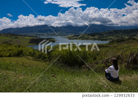 Female tourist sitting looking at the biggest artificial lake in Colombia called Calima Lake located on the mountains of Darien at the region of Valle del Cauca 129932633