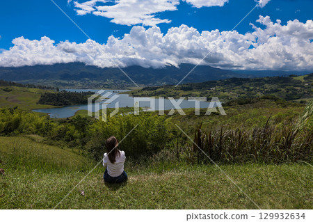Female tourist sitting looking at the biggest artificial lake in Colombia called Calima Lake located on the mountains of Darien at the region of Valle del Cauca 129932634