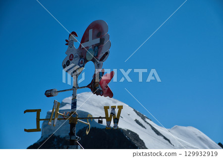 A weather vane erected on an observation deck on a snowy mountain and the summit of the mountain A weather vane erected on an observation deck on a snowy mountain and the summit of the mountain 129932919