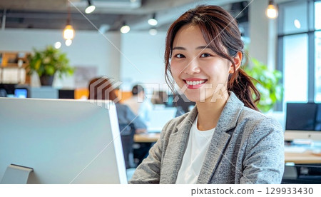 Portrait of a smiling Japanese woman operating a computer in a coworking office 129933430