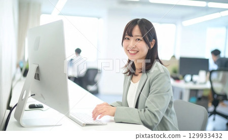 一位微笑的日本女性在聯合辦公室操作電腦的肖像 129933432