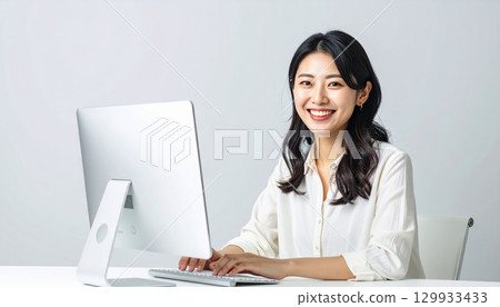 一位日本女性在白色辦公桌上使用電腦工作，淺灰色背景肖像 129933433